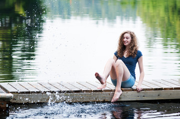 teenage girl sitting on a dock splashing water