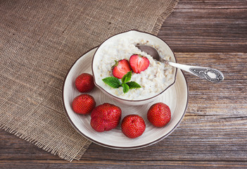 Oatmeal porridge in bowl with fresh strawberries on side. Toned