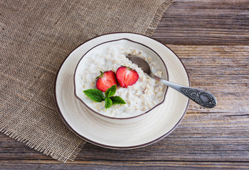 Oatmeal porridge in bowl topped with fresh strawberries on old wooden table