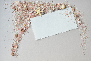 Cockleshells, pink sand and invitation card on a paper background