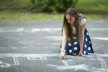 Lovely teen girl draws with chalk on the pavement.