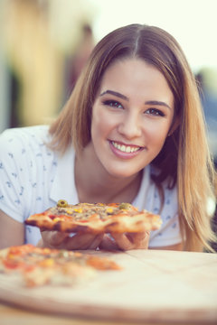 Portrait of cheerful  young woman eating slice of pizza
