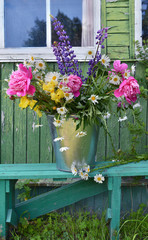 Country still lige with flowers in a bucket on green bench