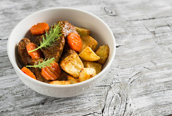 beef goulash with carrots and roasted potatoes in a white bowl on a light wooden background