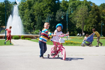 Obraz premium Boy and girl in park learning to ride a bike