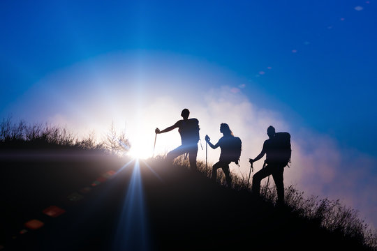 People meeting sunrise on team building session Group of people silhouettes walking toward mountain summit with backpacks hiking trekking gear meeting uprising sun sunbeams and blue sky of background