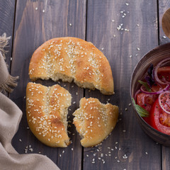 Sesame flat bread with a salad of tomatoes, red onion and basil on the wooden table
