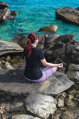 Woman sitting in lotus position, meditating, in from of ocean on sunny day