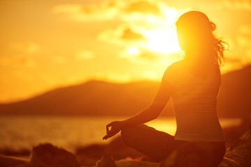 woman meditating in lotus pose on the beach at sunset