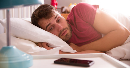 Obraz na płótnie Canvas Man In Bed Woken By Alarm On Mobile Phone