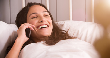 Woman Lying In Bed Having Conversation On Mobile Phone