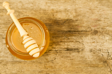jar of fresh honey with drizzler on wooden background, top view