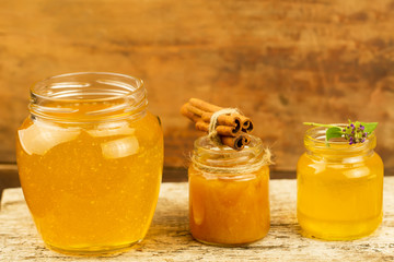 three jars of honey with cinnamon, flowers on wooden background