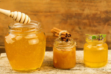 three jars of honey with drizzler, cinnamon, flowers on wooden background