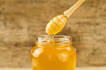 glass jar of honey with drizzler on wooden background