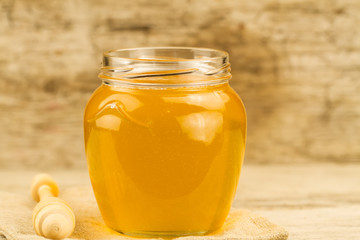 glass jar of honey with drizzler on wooden background