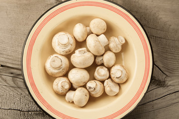 fresh mushrooms on a plate on wooden background, top view