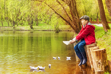 Fototapeta na wymiar Boy alone near pond playing with paper boats