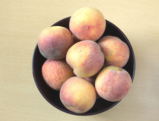 Many appetizing peaches in purple round bowl on wooden background top view