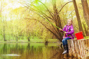Smiling small girl fishing near beautiful pond