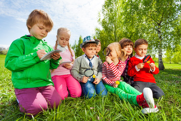 Group of kids sit in the field with magnifier