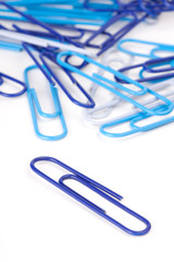 Blue Paper Clips – A blue paper clip in foreground, by itself. Other blue paper clips in background.