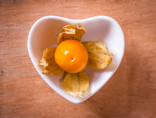 Phys alis, or Cape Gooseberry fruit in the heart bowl and on the wooden background