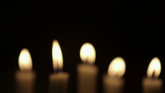 Rack focus on lit candles against black background. Flames are being blown due to wind in studio.

