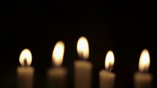 Rack focus on lit candles against black background. Flames are being blown due to wind in studio.
