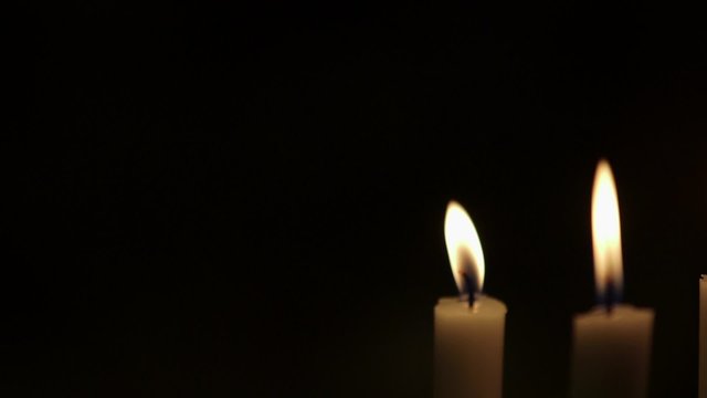 Rack focus on lit candles against black background. Flames are being blown due to wind in studio.
