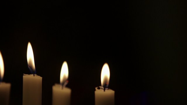 Rack focus on lit candles against black background. Flames are being blown due to wind in studio.
