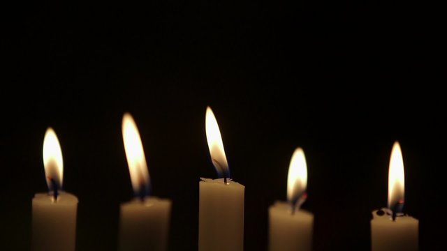 Rack focus on lit candles against black background. Flames are being blown due to wind in studio.

