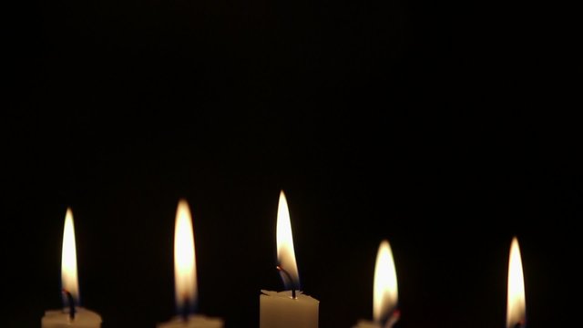 Rack focus on lit candles against black background. Flames are being blown due to wind in studio.
