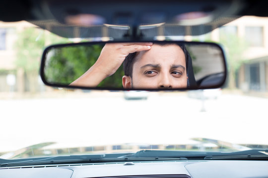 Closeup Portrait, Funny Young Man Driver Looking At Rear View Mirror Looking At Hair Loss Issues Widow's Peak Or Worried, Isolated Interior Car Windshield Background
