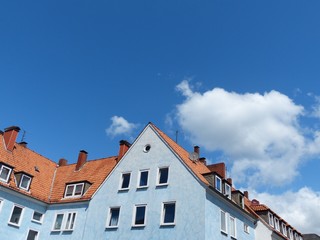 Hellblaue Häuserzeile mit Mansarden und Dachgauben vor blauem Himmel mit weißen Wolken bei...