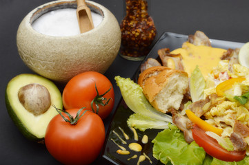 A plate of salad, salt, tomatoes and avocado on a dark background.