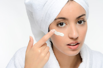 young ethnic woman in white peignoir putting on skincare facial cream