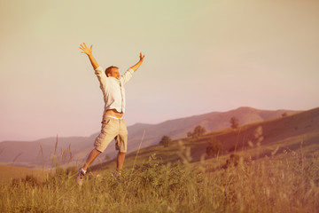 Guy with Outstreched arms jump in a green grass meadow in a mountain