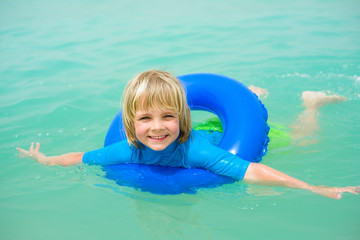 Happy little boy  with blue life ring has fun in the water