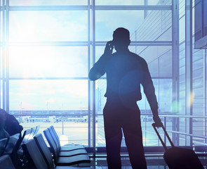 Geschäftsreisender mit Koffer telefoniert im Flughafen
