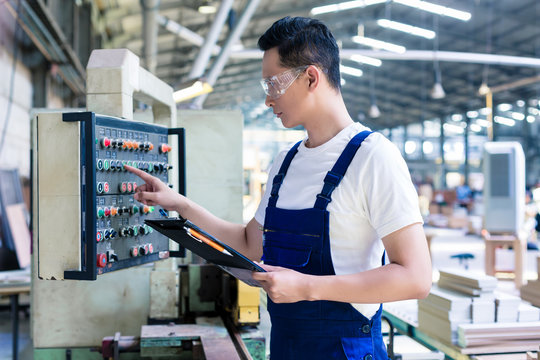 Worker pressing buttons on CNC machine in factory
