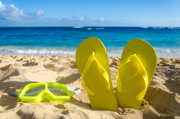 Yellow flip flops with swim glasses on the sandy beach