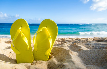 Obraz premium Yellow flip flops on the sandy beach