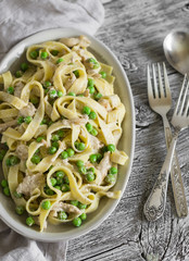 homemade pasta with green peas, chicken breast and cream sauce on a light wooden surface
