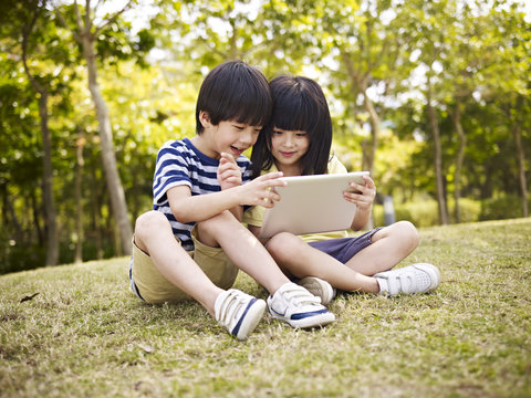 two asian children using tablet outdoors