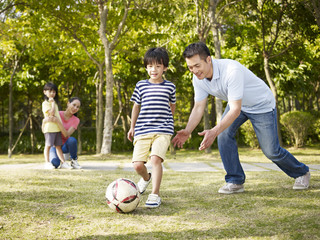 father coaching son to play soccer in park