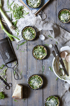 group of little quiche with green fresh herbs and Parmesan cheese on wooden table