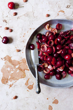 cutting in half juicy cherries on a round tray on marble surface with a knife