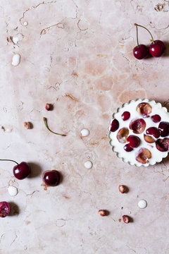 little clafoutis with juicy cherries on mold on pink marble surface with whole cherries