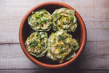 Cooked artichokes with parsley and parmesan, served in a clay dish on a wooden table